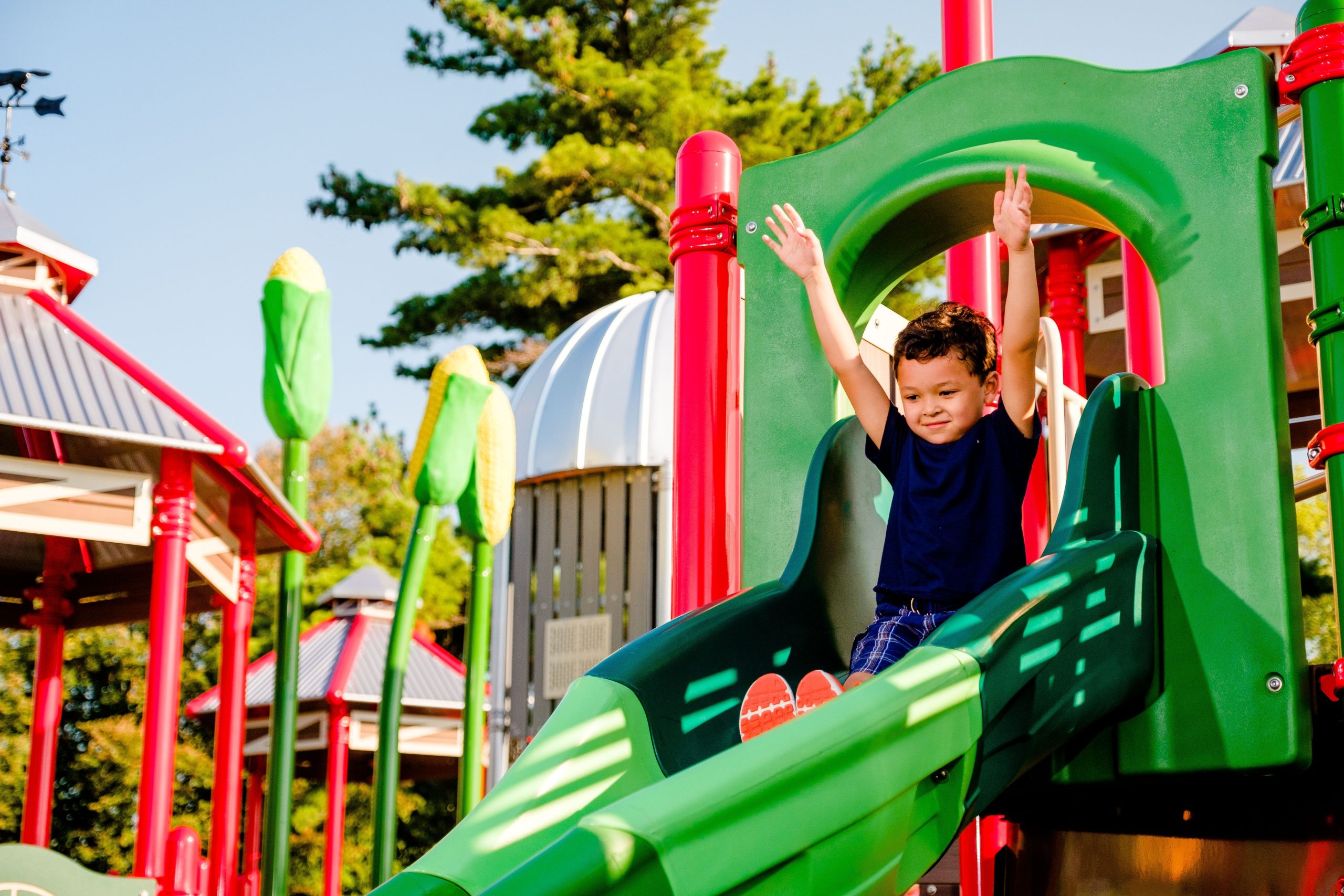 boy going down commercial playground slide with his hands up